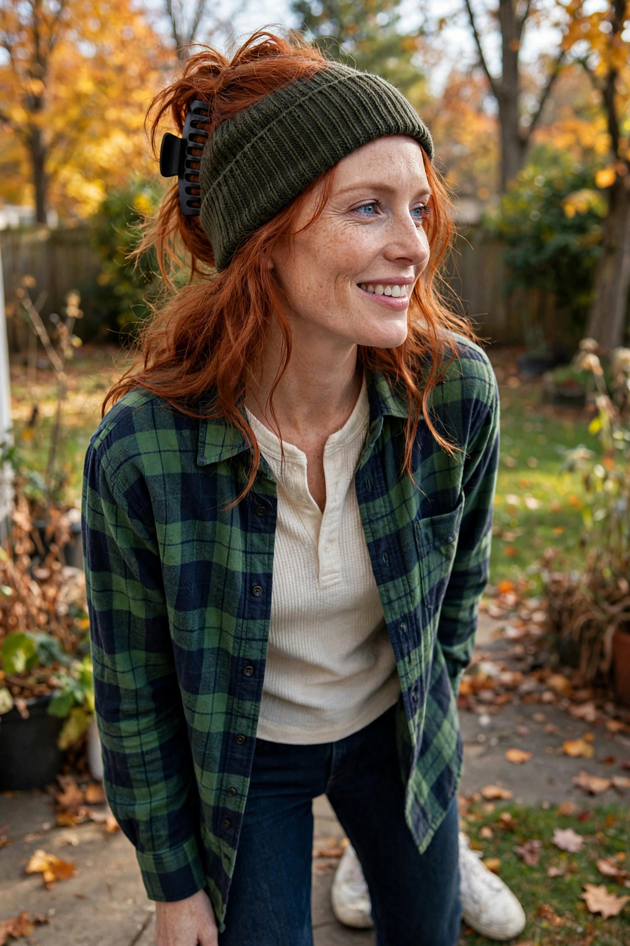 Woman in a flannel shirt and jeans with a beanie in a backyard